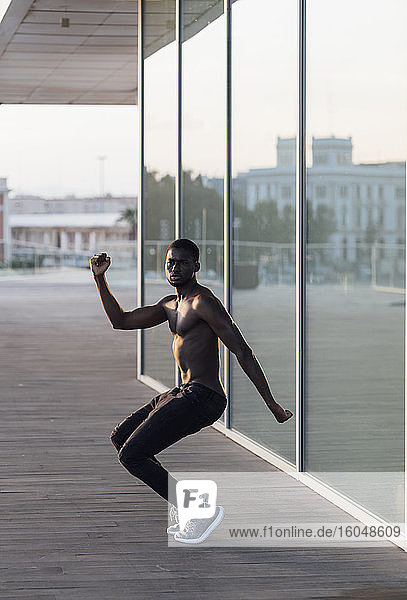 Young shirtless man dancing by window glass