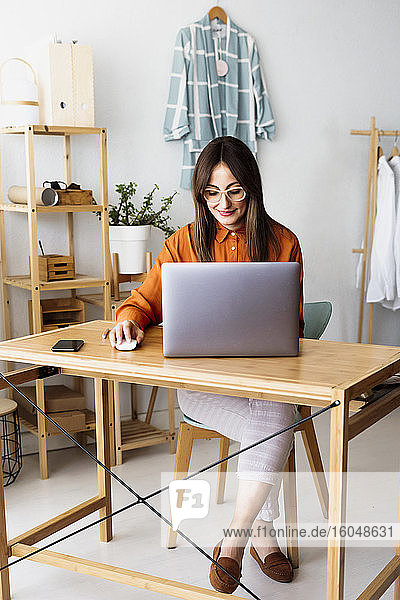 Modedesignerin arbeitet zu Hause am Schreibtisch mit Laptop