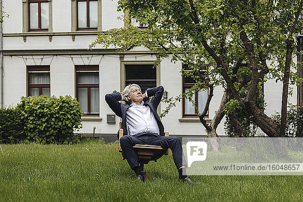 Entspannter älterer Geschäftsmann  der auf einem Stuhl in einem ländlichen Garten sitzt und nach oben schaut