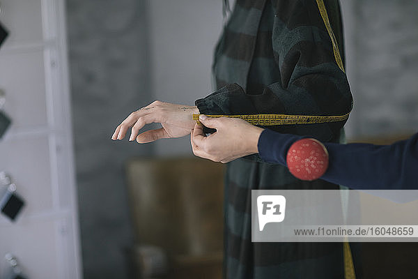 Abgeschnittene Hände eines Schneiders  der die Hand einer Frau im Designstudio misst
