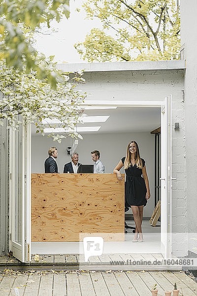 Geschäftsfrau steht in offener Bürotür  Menschen arbeiten im Hintergrund