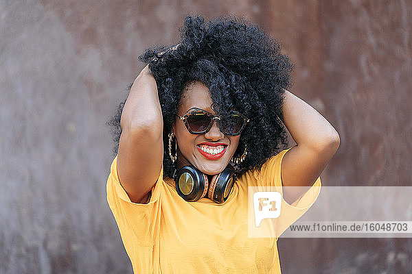 Lächelnde Frau mit Afro-Haar und Sonnenbrille und Händen im Haar