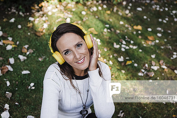 Glückliche schöne Frau hört Musik  während sie im Park sitzt