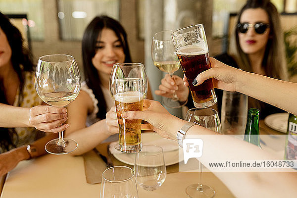 Glückliche Freundinnen stoßen mit Getränken an  während sie am Tisch im Restaurant sitzen