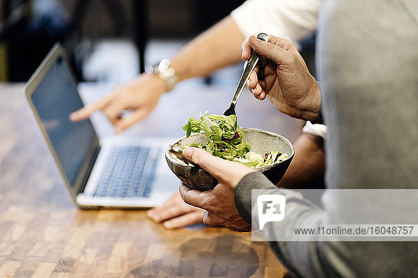 Mann hält Schüssel mit Salat  während der andere auf einen Laptop zeigt