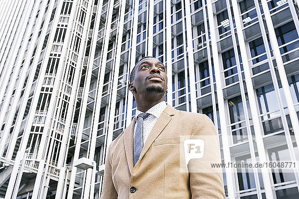 Junger Geschäftsmann vor einem modernen Bürogebäude in der Stadt  der zur Seite schaut