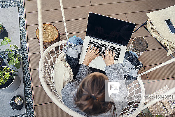 Junge Frau benutzt einen Laptop  während sie auf einer Schaukel im Garten sitzt