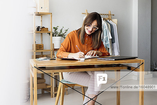 Female fashion designer working at home sitting at desk taking notes