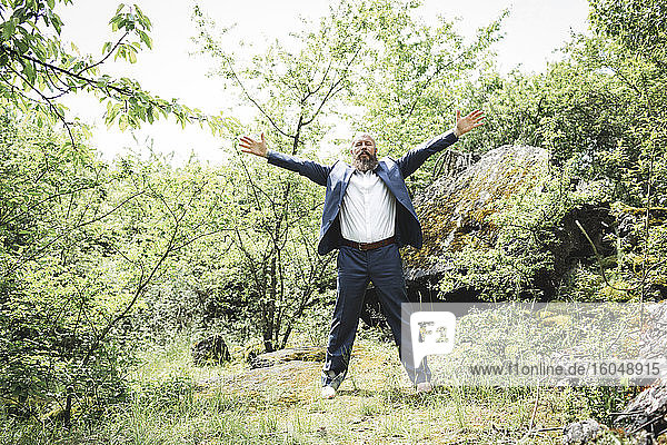 Bearded businessman with arms outstretched exercising on land in forest