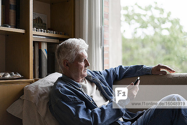 Senior man using smart phone while relaxing on sofa at home