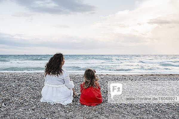 Mutter und Tochter entspannen sich am Strand bei bewölktem Himmel