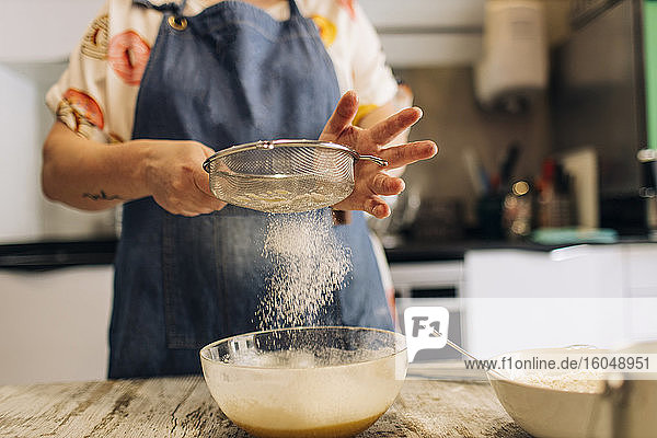 Nahaufnahme einer Bäckerin beim Sieben von Mehl in Teig auf einem Tisch in einer Werkstatt