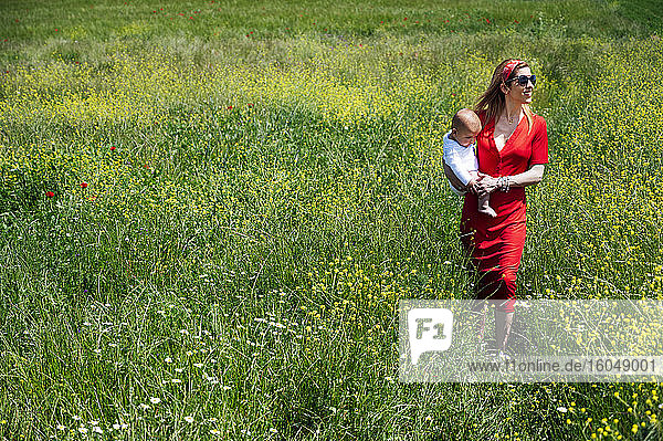 Frau trägt ihren kleinen Sohn bei einem Spaziergang auf einer Wiese an einem sonnigen Tag