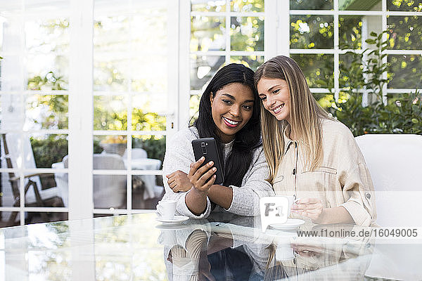 Happy multi-ethnic female friends taking selfie through smart phone at table in coffee shop