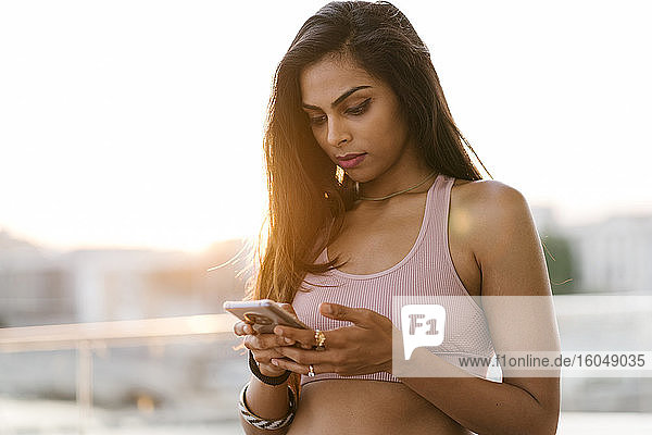 Close-up of sportswoman using smart phone while standing against clear sky at sunset