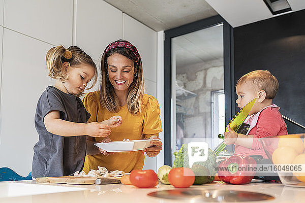 Mutter und Mädchen bereiten Essen zu  während die kleine Tochter auf der Kücheninsel sitzt