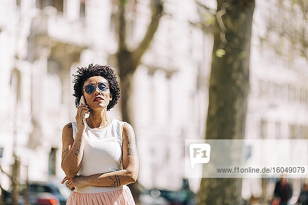 Frau mit Sonnenbrille  die über ein Smartphone spricht  während sie in der Stadt steht
