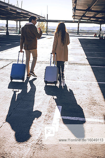 Business-Paar zieht Gepäck beim Gehen auf dem Flughafenparkplatz während des sonnigen Tages