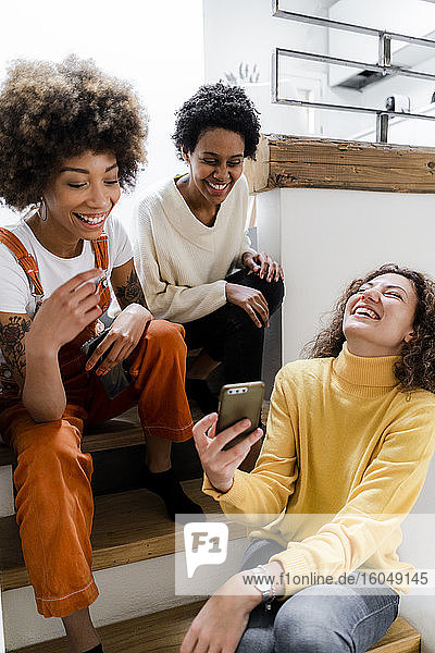 Drei lachende junge Frauen haben Spaß mit dem Smartphone zu Hause