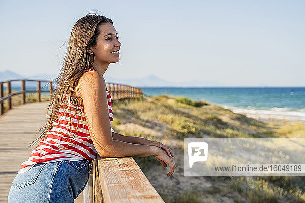 Nachdenkliches Teenager-Mädchen auf der Promenade am Strand gegen den klaren blauen Himmel stehend