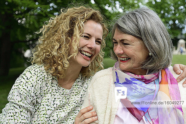 Cheerful blond woman looking at senior woman in park
