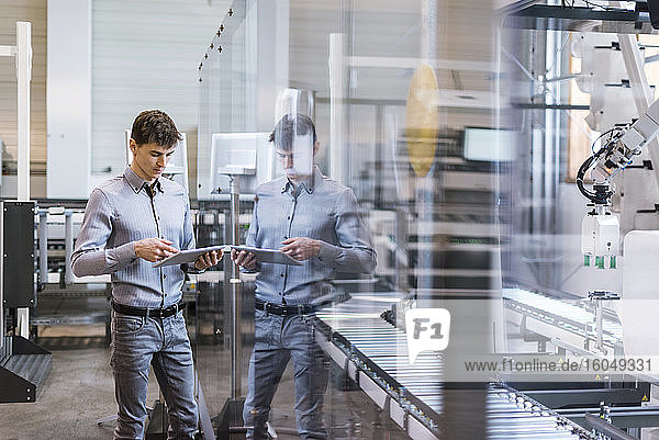 Männlicher Fachmann  der ein digitales Tablet benutzt  während er in einer Fabrik am Fließband steht