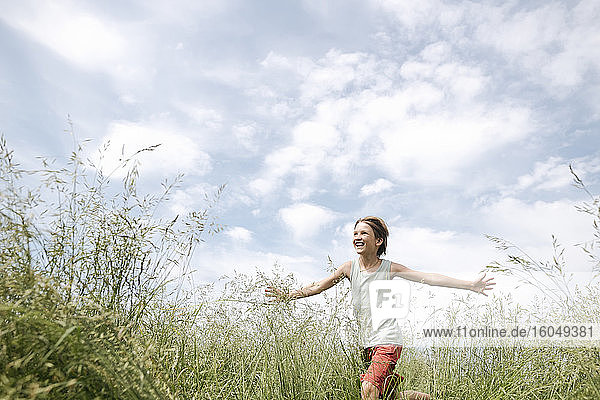 Portrait of happy boy running on a field with arms outstretched