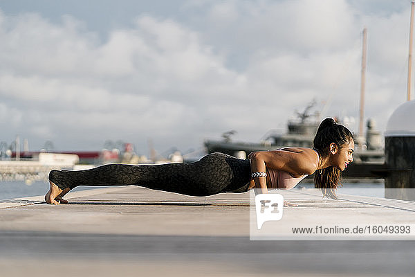 Weibliche Athletin übt vierbeinige Stab-Pose auf dem Pier am Hafen