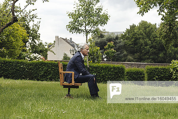 Älterer Geschäftsmann sitzt auf einem Stuhl in einem ländlichen Garten