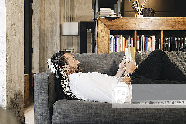 Mature man lying on couch  relaxing  reading book
