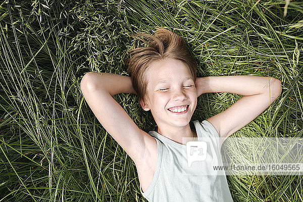 Porträt eines glücklichen Jungen mit geschlossenen Augen  der im Sommer auf einer Wiese liegt