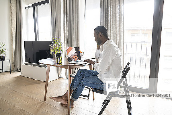Mann sitzt am Tisch in einer modernen Wohnung und benutzt einen Laptop