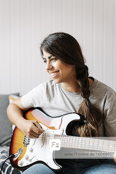 Happy woman playing electric guitar while sitting at home