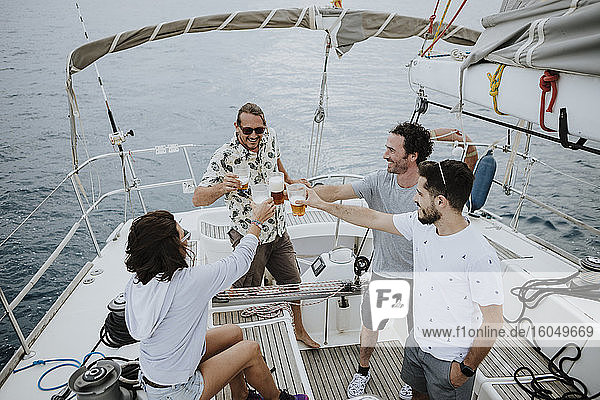 Freunde stoßen mit Bier an  während sie auf einem Segelboot im Meer sitzen