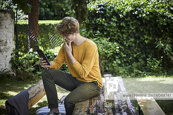 Young man sitting on beer table in garden using digital tablet
