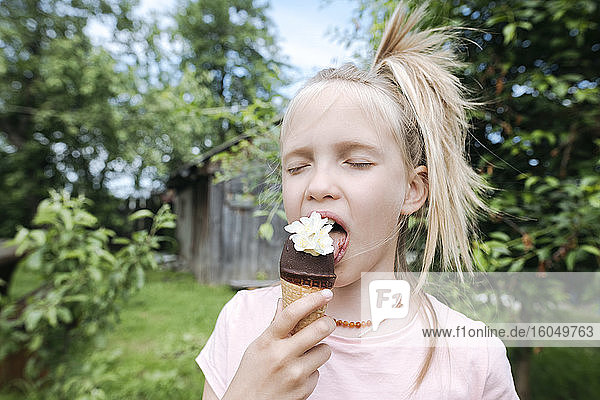 Porträt eines blonden Mädchens mit geschlossenen Augen  das Eis mit Jasminblüten im Garten isst
