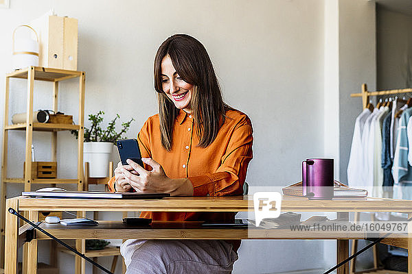 Modedesignerin  die zu Hause am Schreibtisch sitzt und ein Smartphone benutzt
