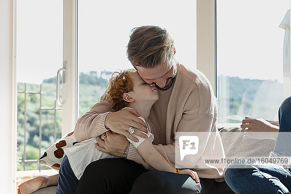 Man embracing cute preschool son while sitting by woman in living room at home