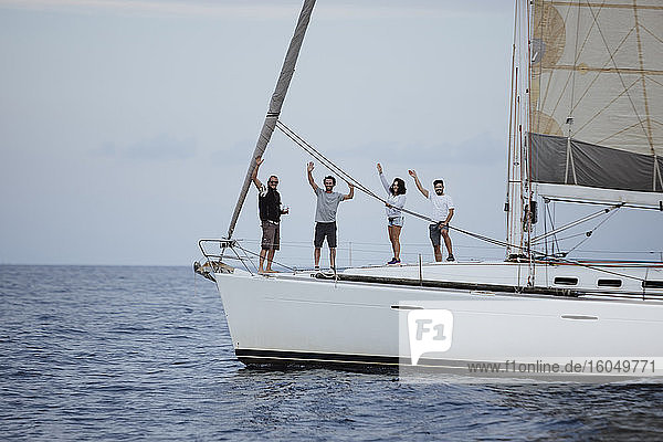 Glückliche Freunde winken  während sie auf einem Segelboot im Meer stehen