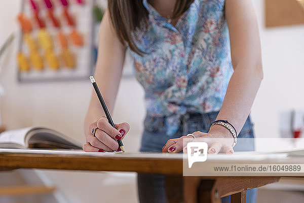 Junge weibliche Auszubildende  die an einer Werkbank im Atelier einen Entwurf zeichnet