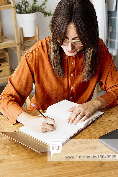 Freiberuflerin  die zu Hause am Schreibtisch sitzt und Notizen macht