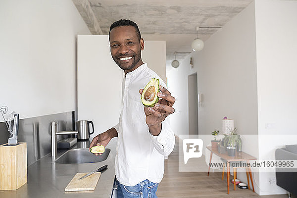Porträt eines lächelnden Mannes mit geschnittener Avocado in seiner Küche