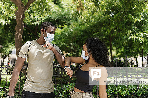 Mann und Frau tragen Masken  während sie sich im Park mit den Ellbogen berühren