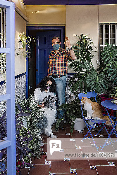 Mann mit Maske winkt mit der Hand  während Frau Hund im Hof streichelt