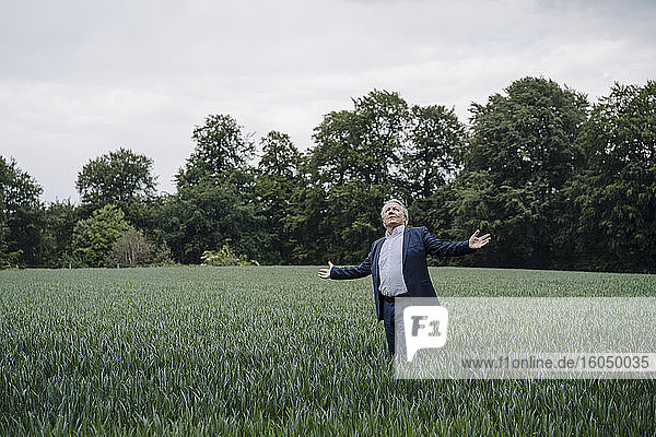 Senior businessman standing on a field in the countryside with outstretched arms