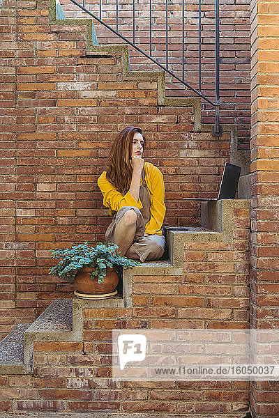 Gelangweilte nachdenkliche Frau mit Laptop und Smartphone auf den Stufen sitzend