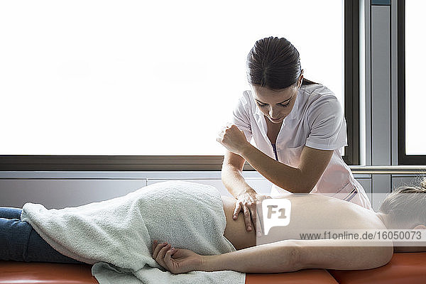Die Hände einer Physiotherapeutin massieren den Rücken einer Frau