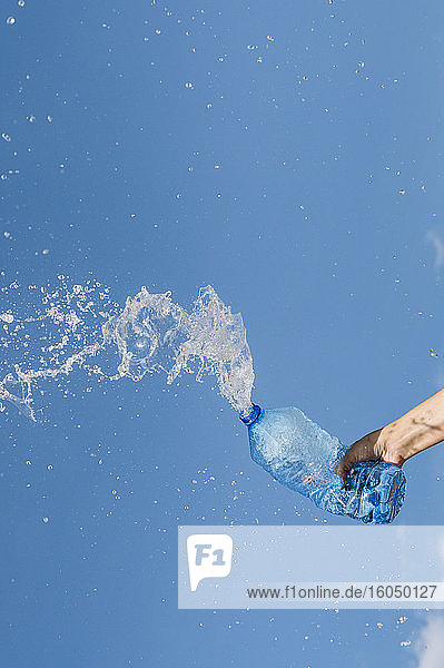 Hand einer Frau  die Wasser aus einer Flasche gegen den blauen Himmel spritzt