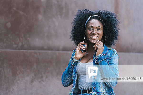 Lächelnde Frau mit Afro-Haar und Kopfhörern schaut in die Kamera