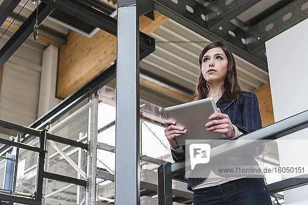 Geschäftsfrau hält digitales Tablet und schaut weg  während sie in einer Fabrik steht